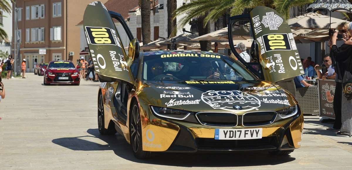 A gold BMW i8 rally car with its doors raised at the 2017 Gumball 3000 stop in Montenegro.