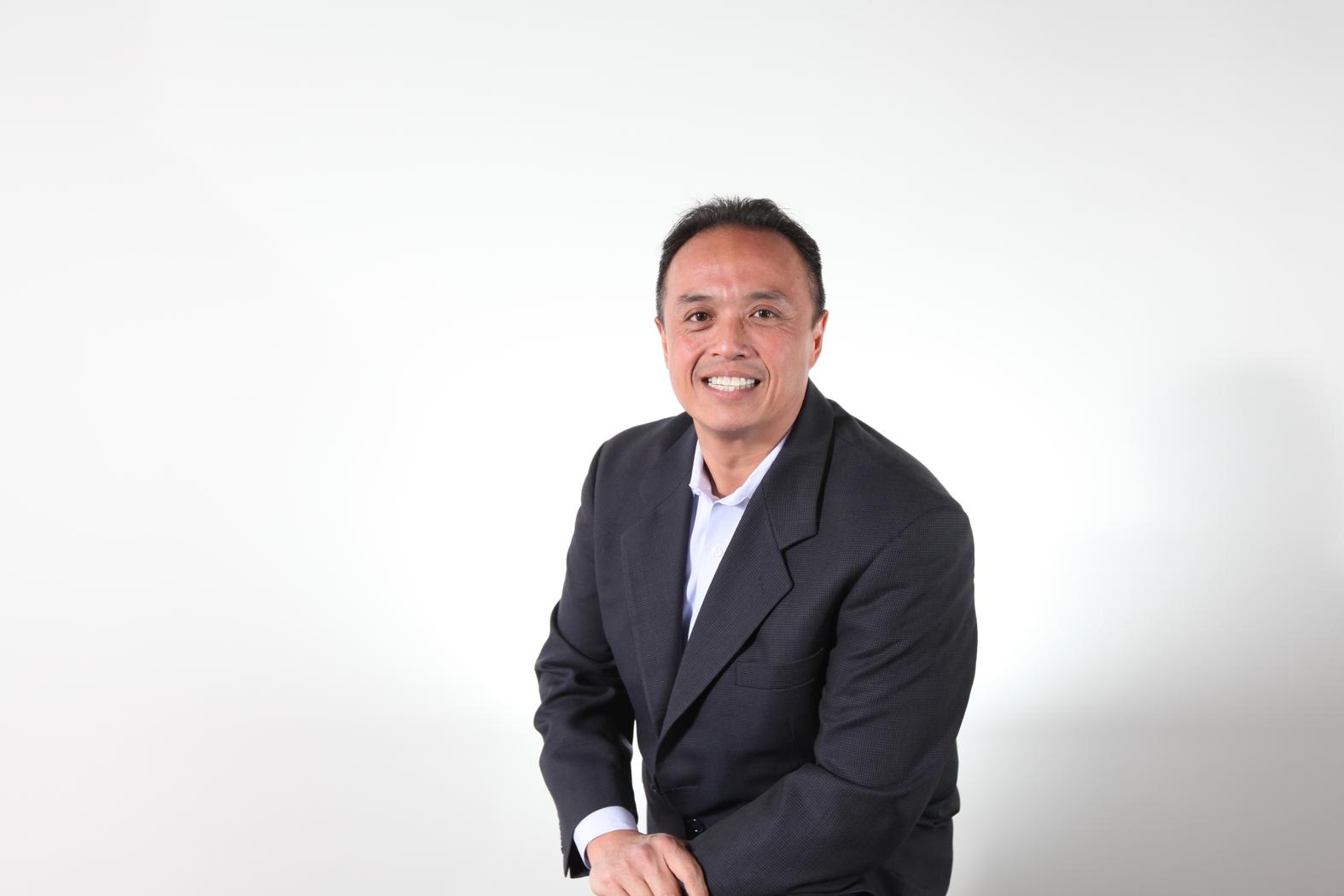 Arnold Magcale seated in a dark jacket against a pale studio background