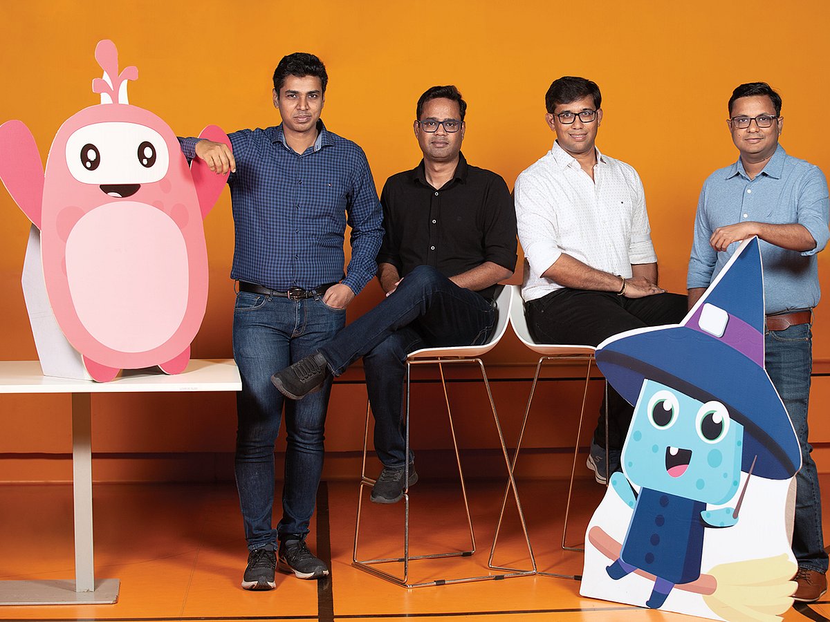 SplashLearn co-founders Arpit Jain, Umang Jain, Joy Deep Nath and Mayank Jain standing together with two colorful learning mascots