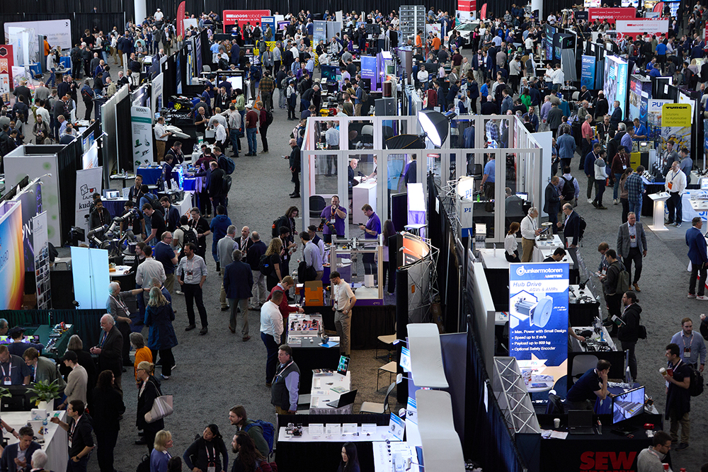 An overhead view of a crowded Robotics Summit exhibition floor with booths and attendees