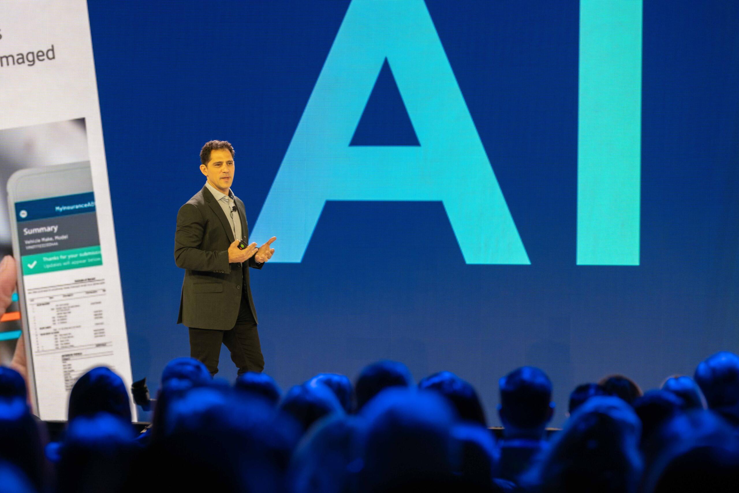 Art Papas speaking on a conference stage beside a large AI graphic