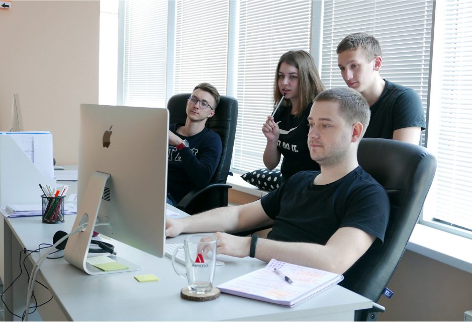 Artezio team members gathered around a desktop computer