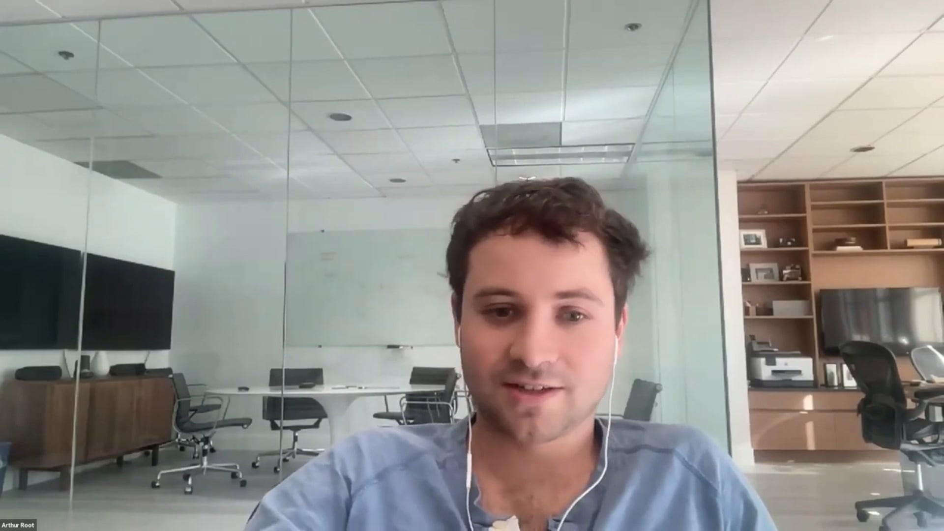 Arthur Root wearing earphones while taking part in an Ecomm.Stream video conversation from a glass-walled office