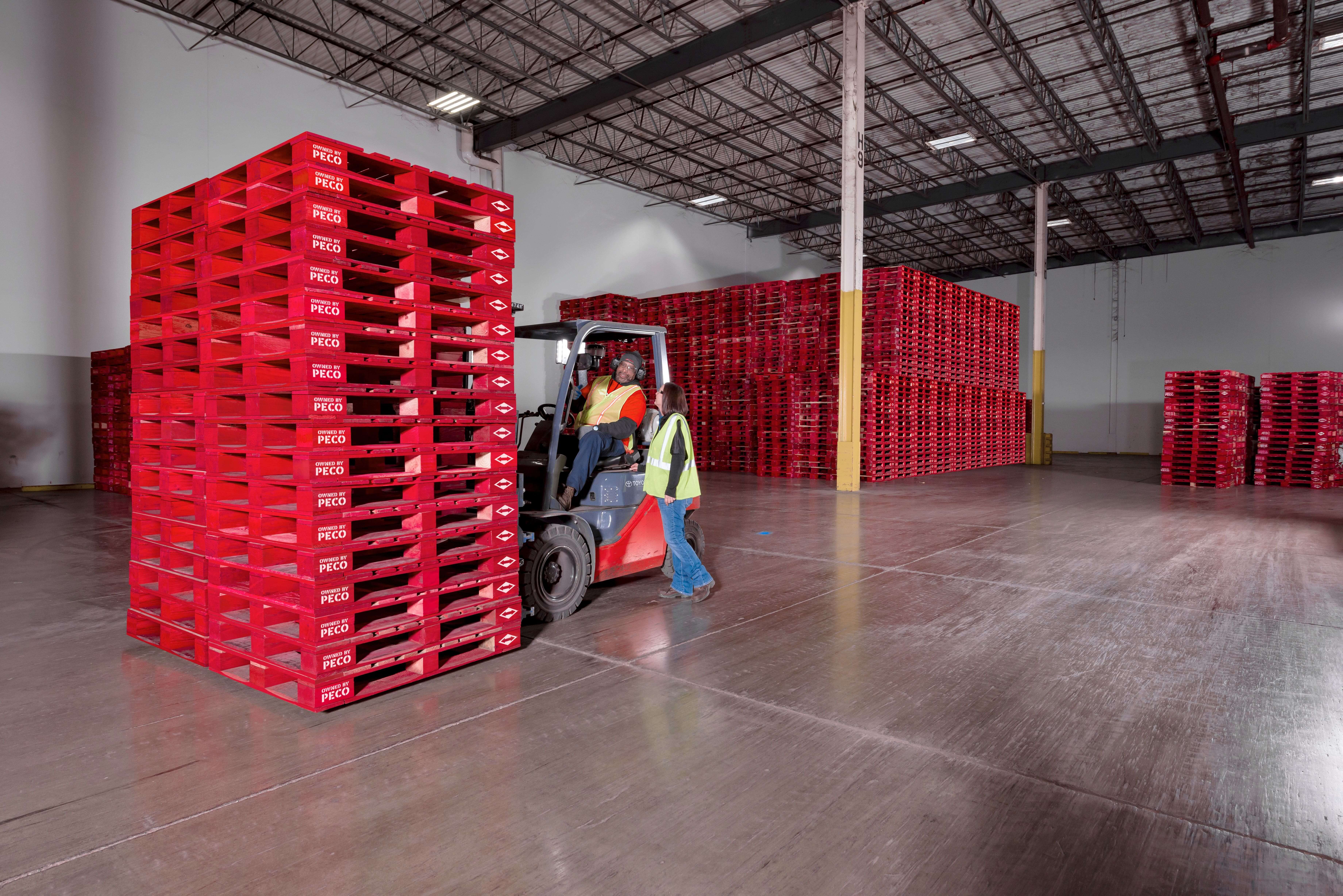 Stacks of red PECO pallets beside a forklift inside a warehouse