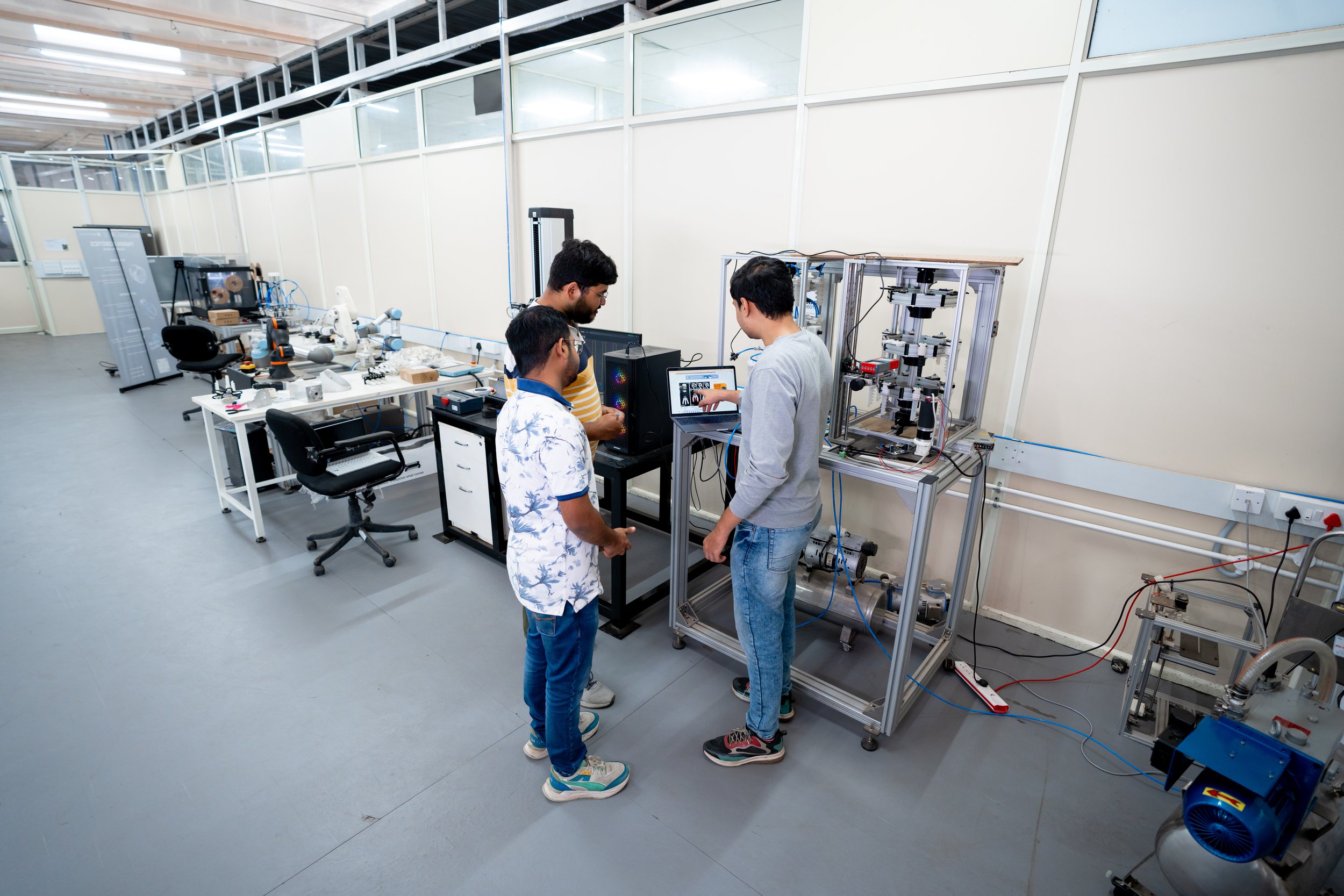 Three people examining equipment and a computer in ARTPARK’s robotics workspace