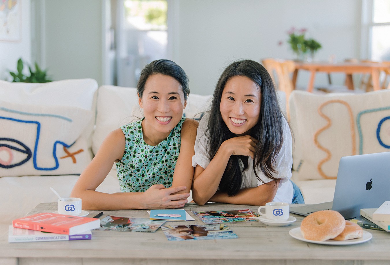 Dawoon and Arum Kang sitting together at a table with coffee, bagels and a laptop