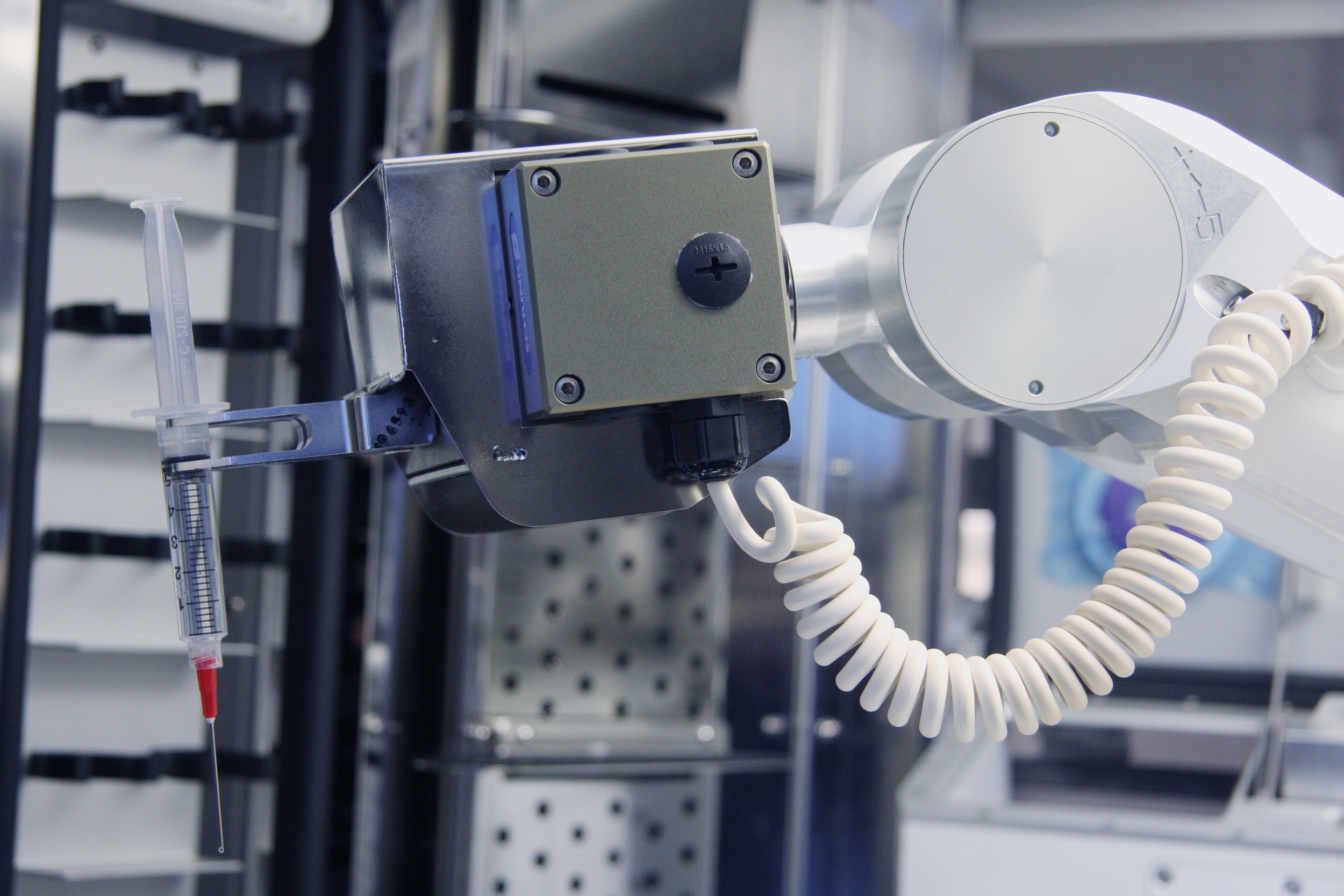 Close-up of the RIVA robotic arm holding a syringe inside the compounding system