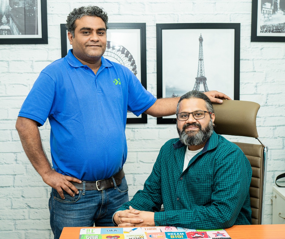 Asad Khan, standing in a blue shirt, with co-founder Jay Singh seated in their office