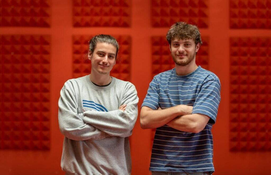 Apply Design co-founders Yaniv Knoll and Asaf Amit standing in front of a vivid orange wall