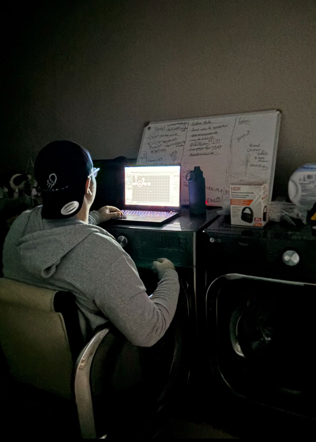 Spaceium co-founder Reza Fetanat working at a laptop in the cramped early apartment workspace beside a dryer and whiteboard