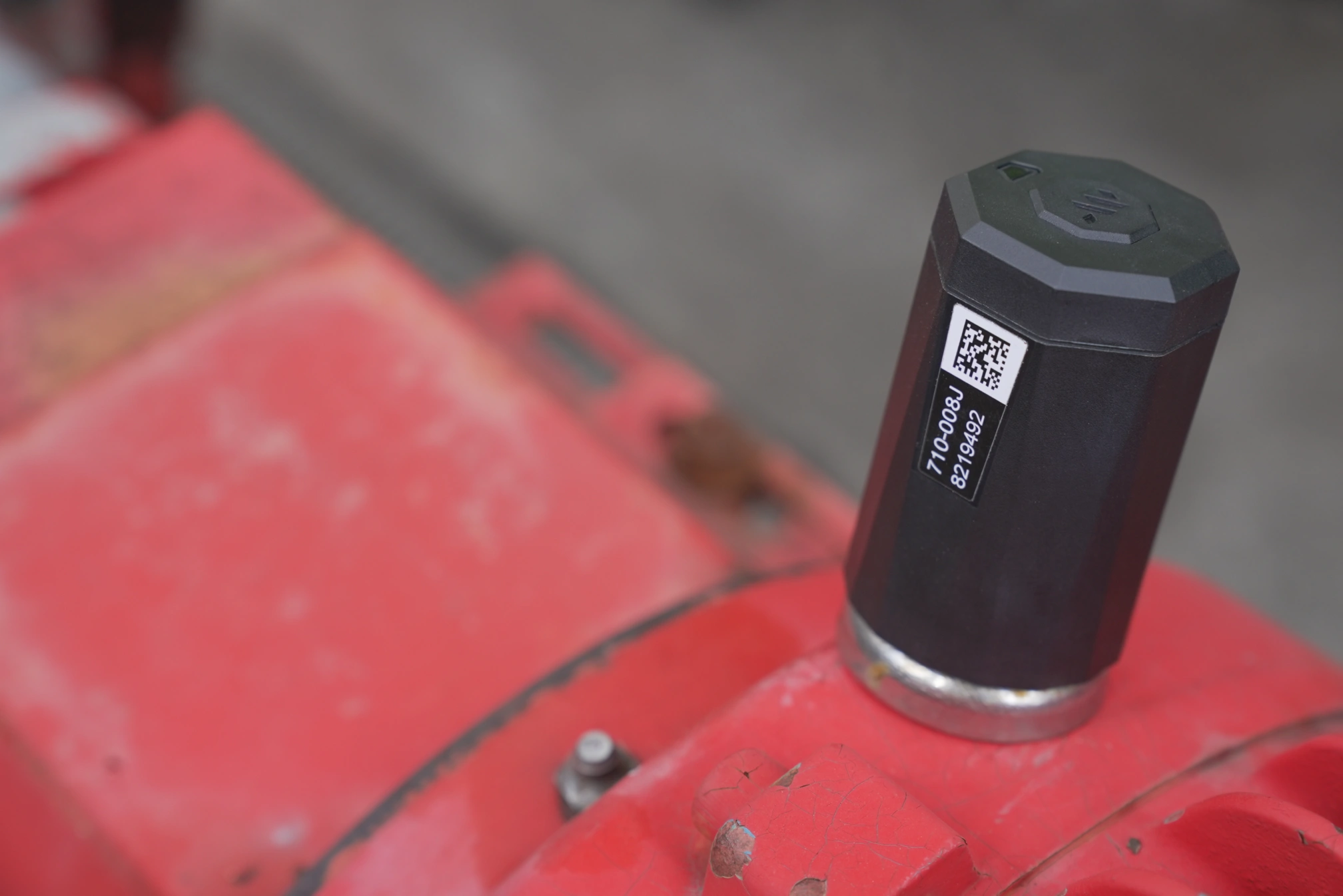 A black wireless condition-monitoring sensor mounted on red industrial machinery