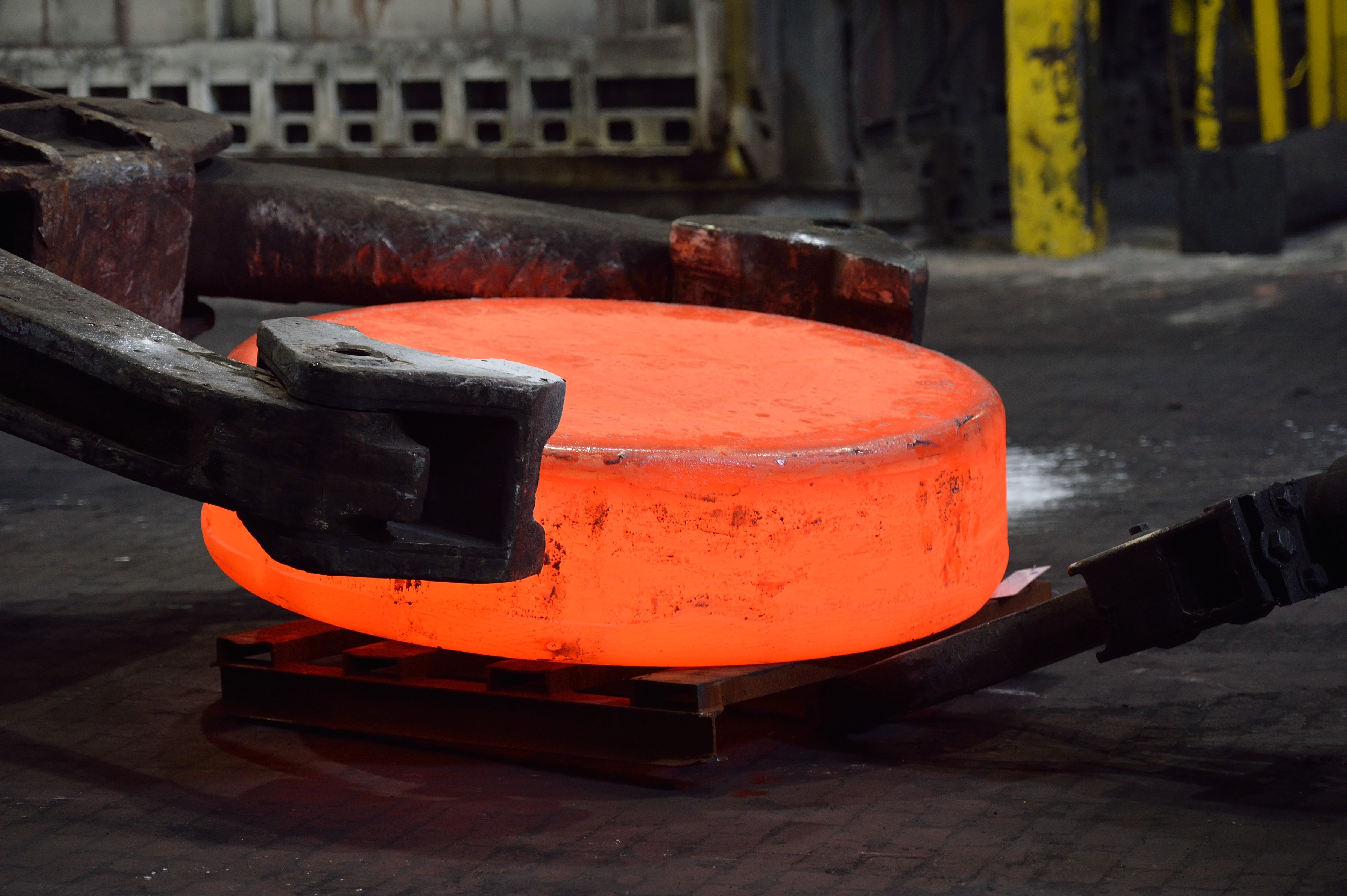 A glowing orange metal workpiece held by heavy industrial handling equipment at ATI’s forging operation