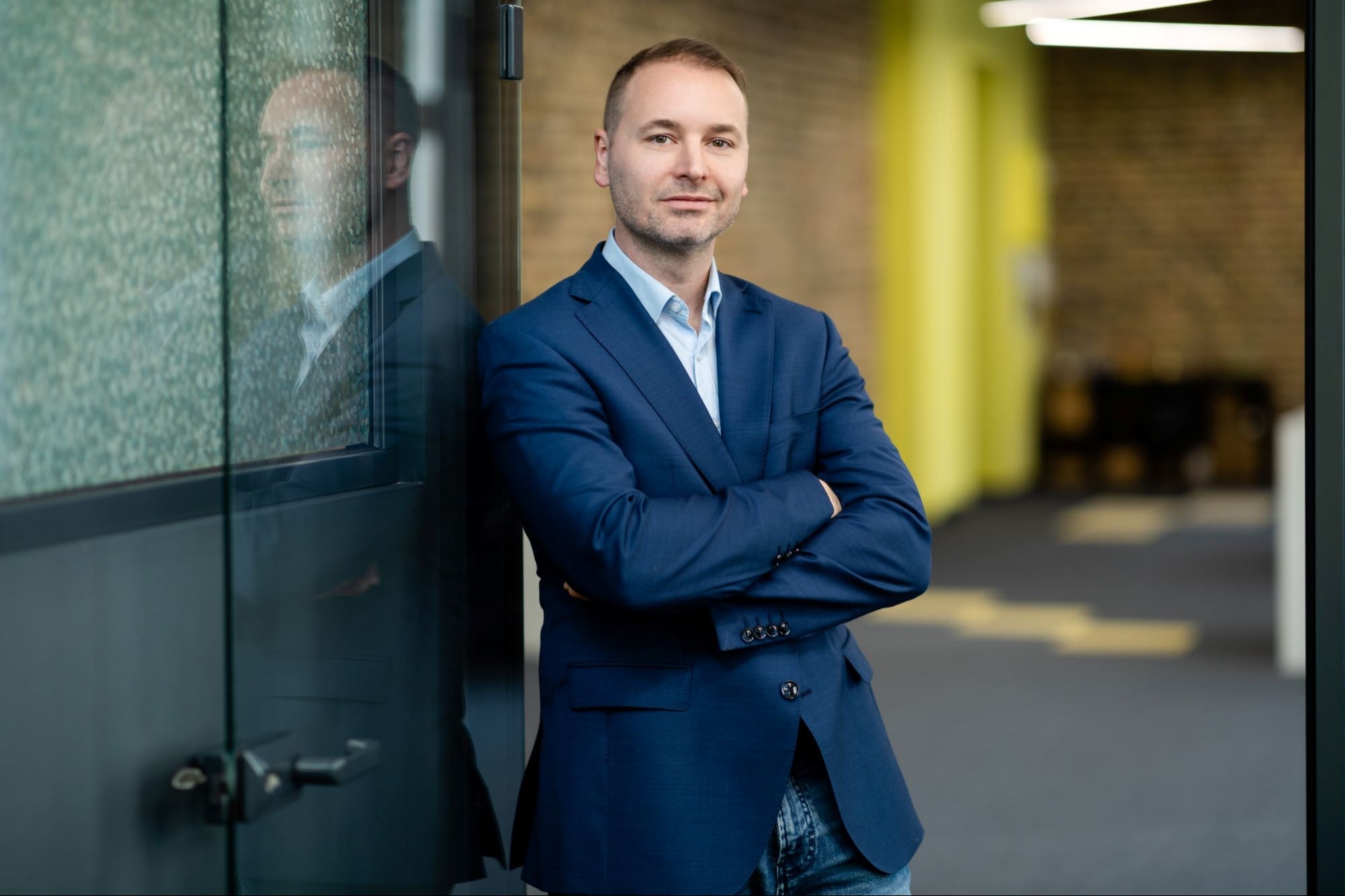 Attila Kecsmar standing with folded arms beside a glass office wall