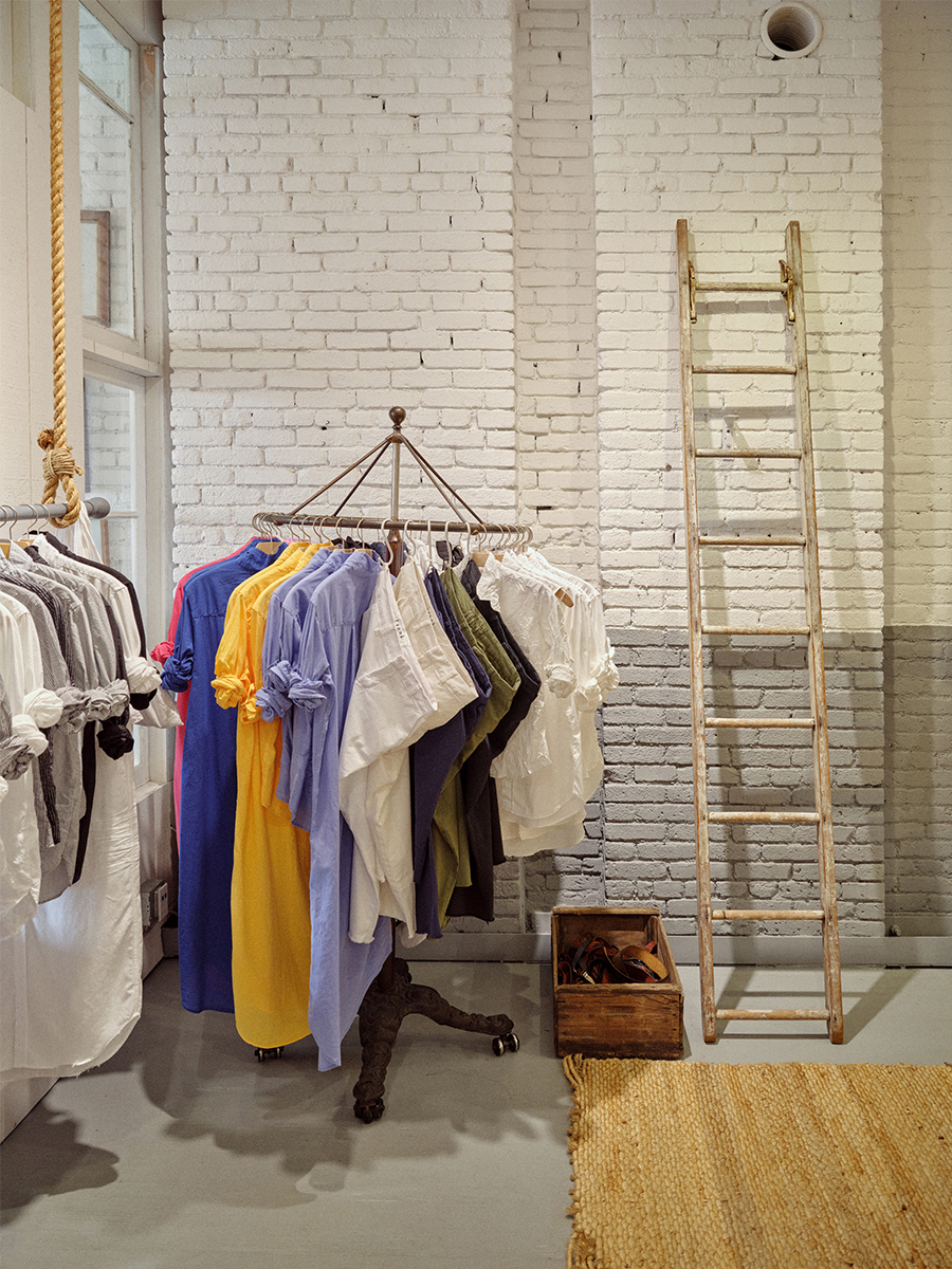 A rack of relaxed Frank & Eileen shirts in white, yellow, blue and green against a white brick wall