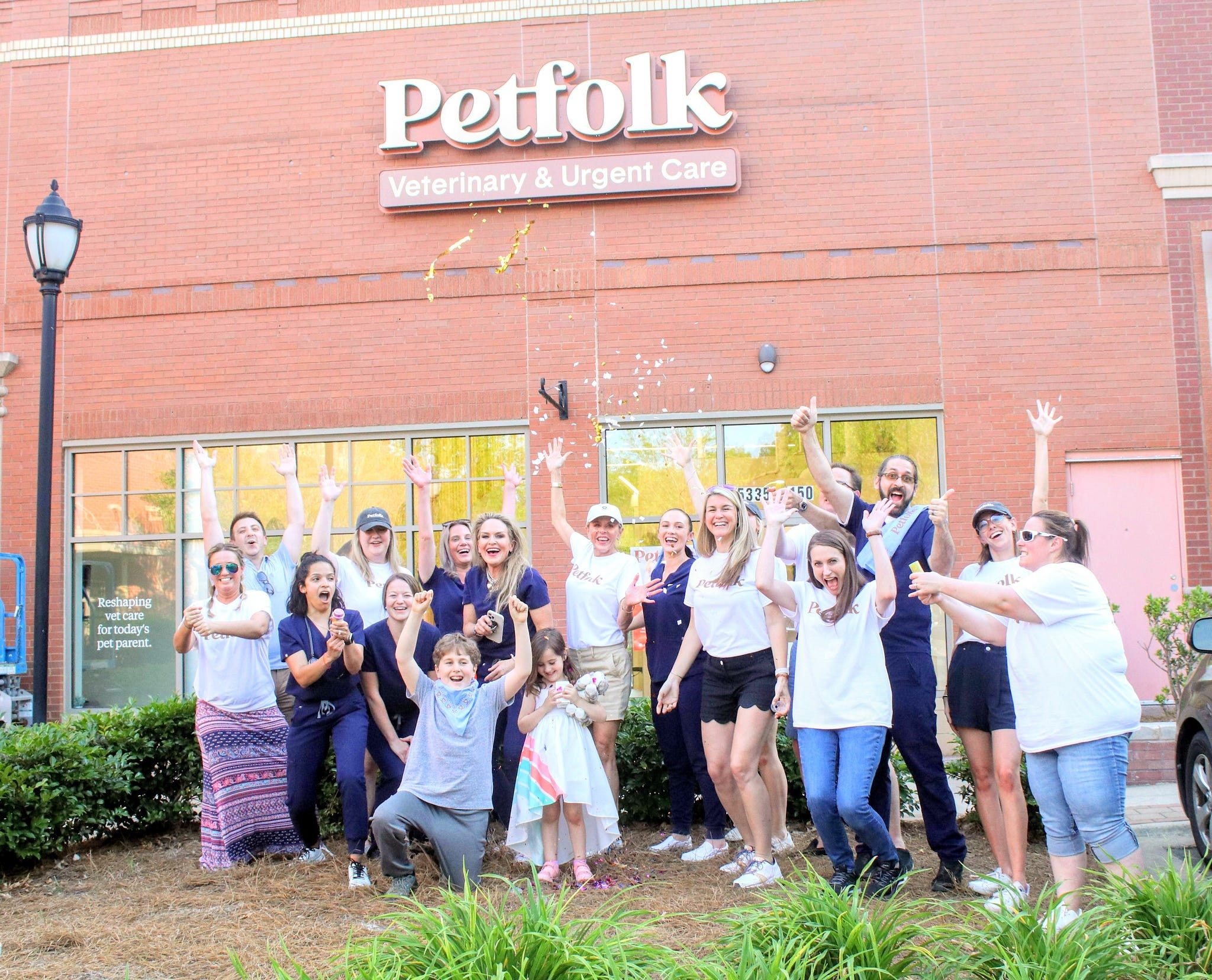 Audrey Wystrach with a group celebrating outside a Petfolk location, arms raised as confetti falls