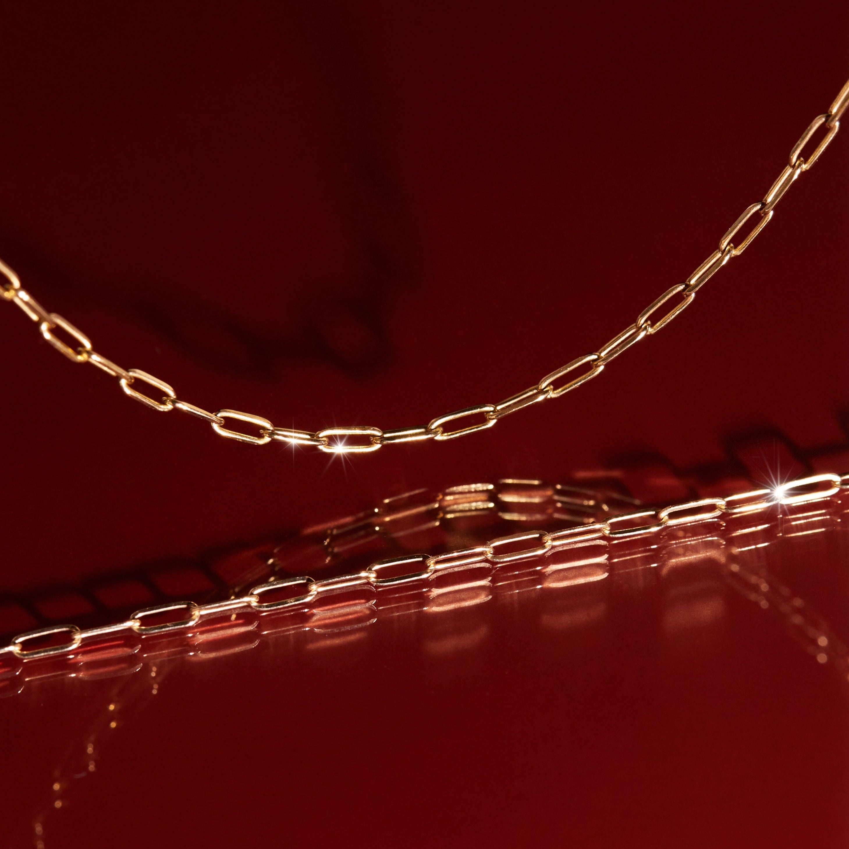 Aurate gold paperclip chain photographed against a deep red background