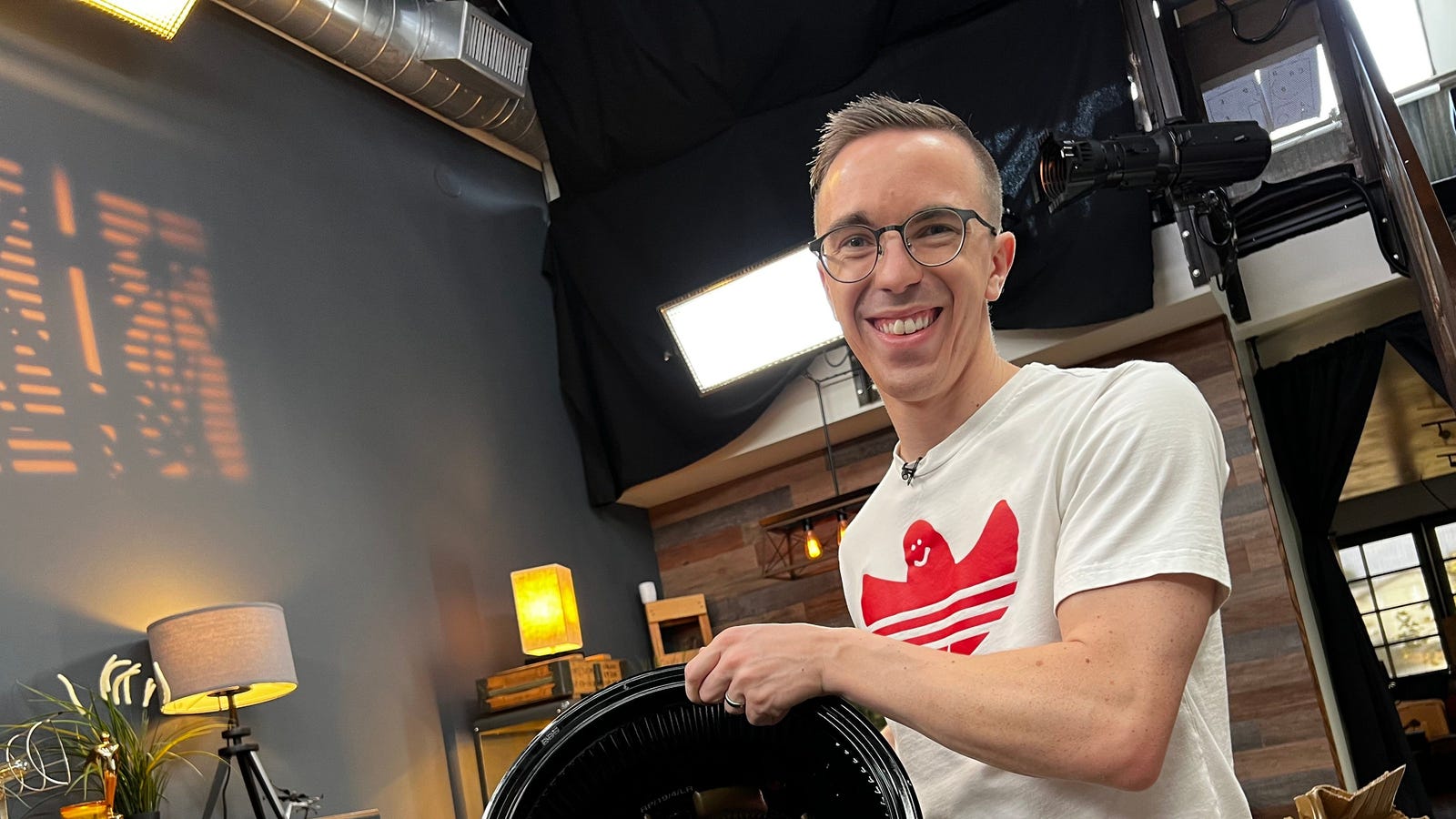 Austin Evans in a production studio, holding a large camera lens