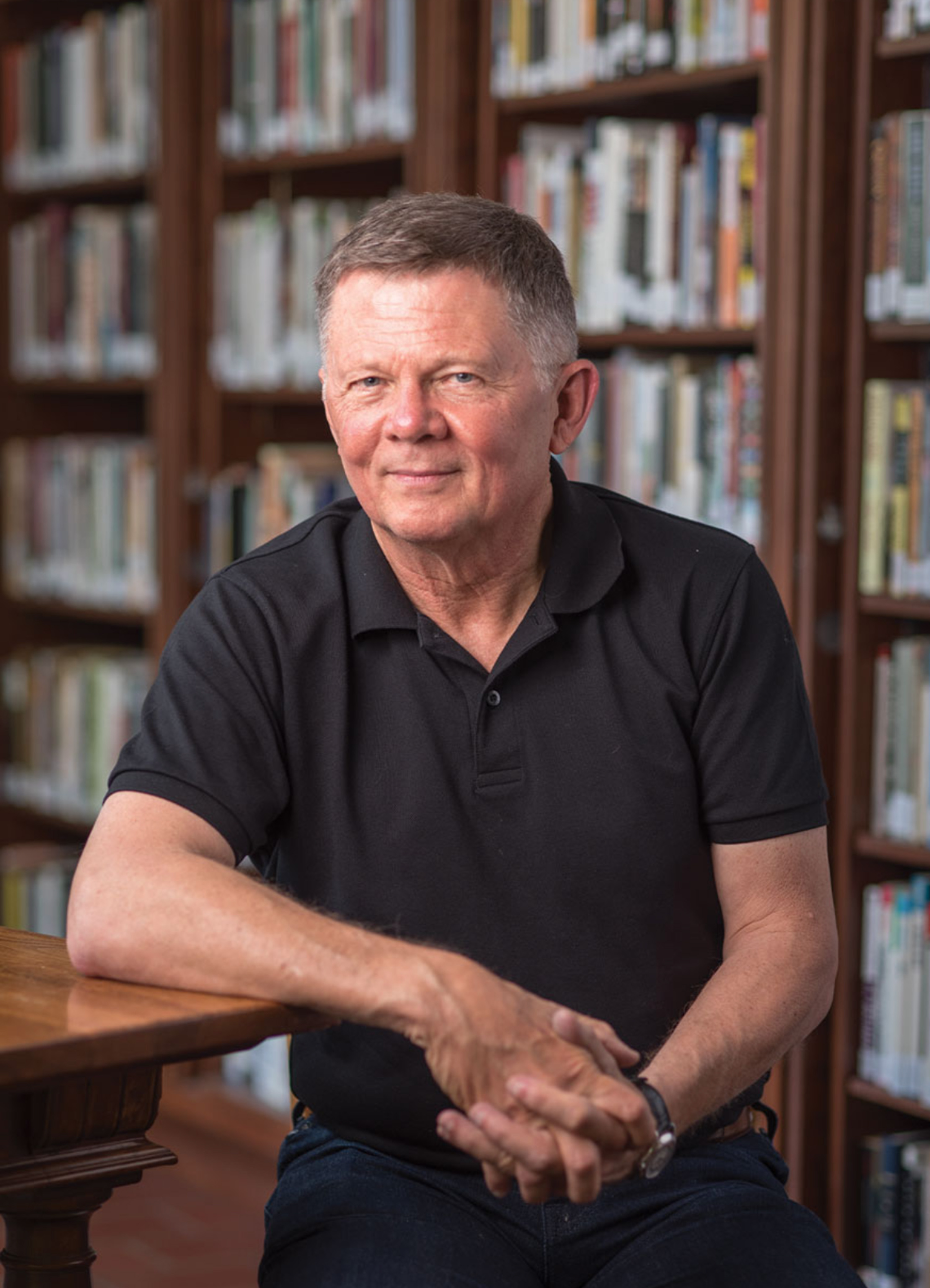 Austin Ligon seated at a wooden table in front of bookshelves