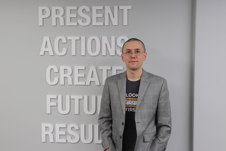 Austin Mac Nab standing beside office wall lettering about present actions and future results