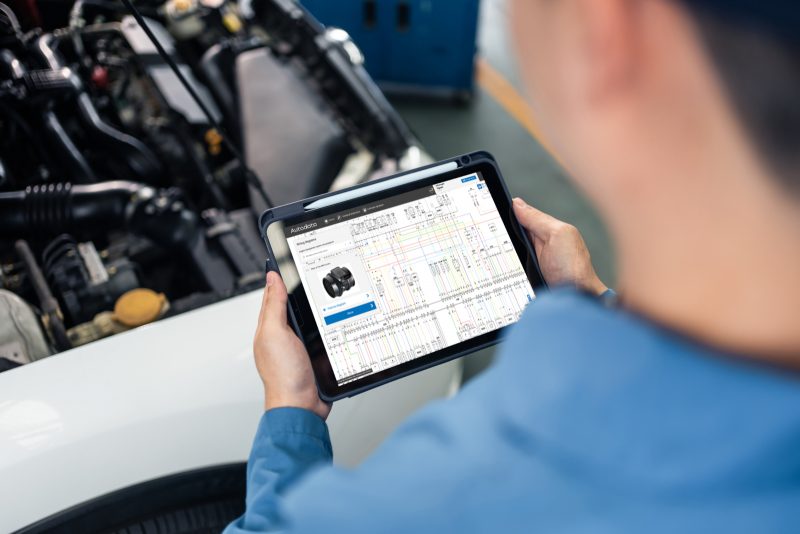 Technician consulting an Autodata wiring diagram on a tablet beside an open car bonnet