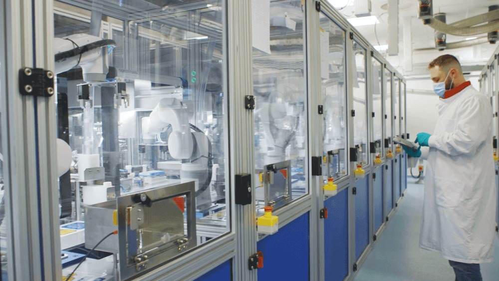 A laboratory worker uses a tablet beside Eva robotic arms at an NHS Southampton testing lab