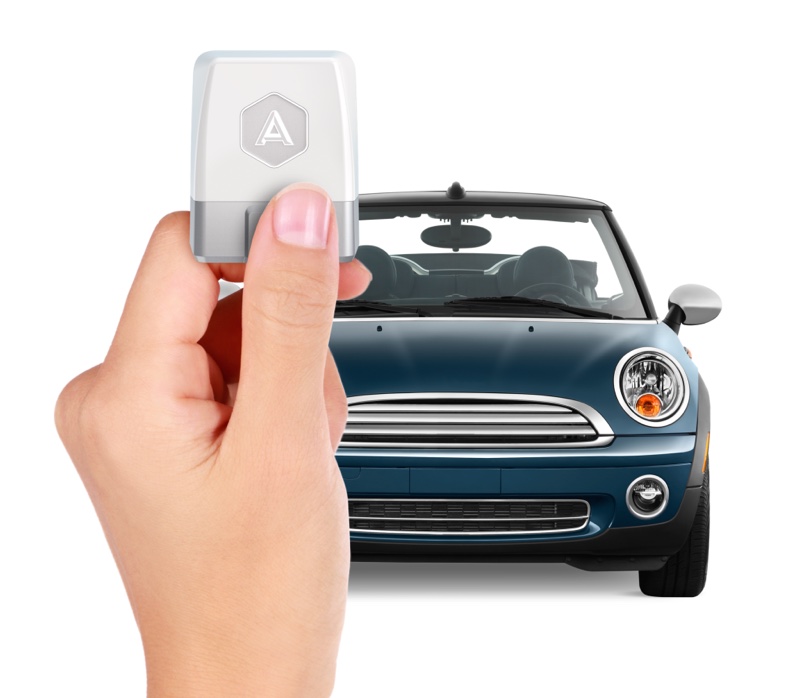 A hand holds a second-generation Automatic adapter in front of a blue Mini convertible