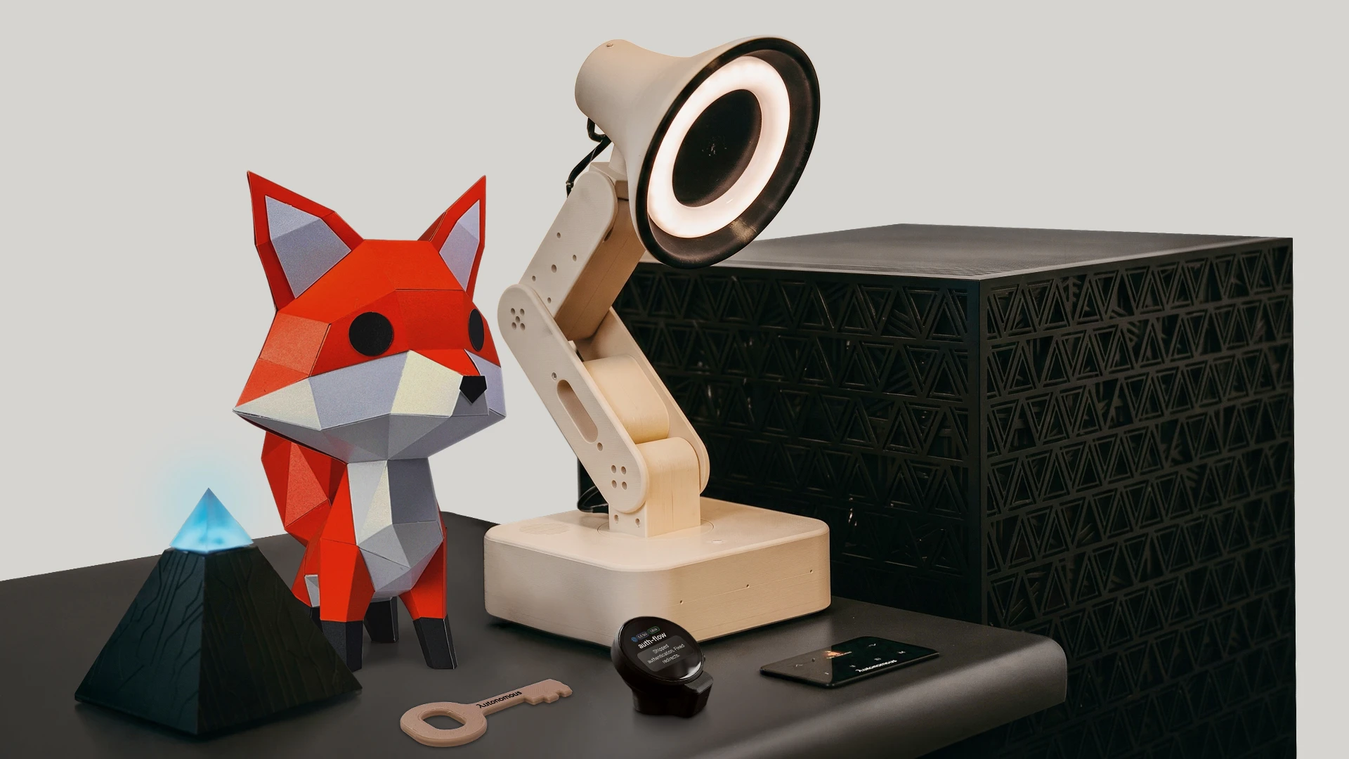 Autonomous AI hardware lineup including a robotic lamp, a paper fox mascot, and a black computer