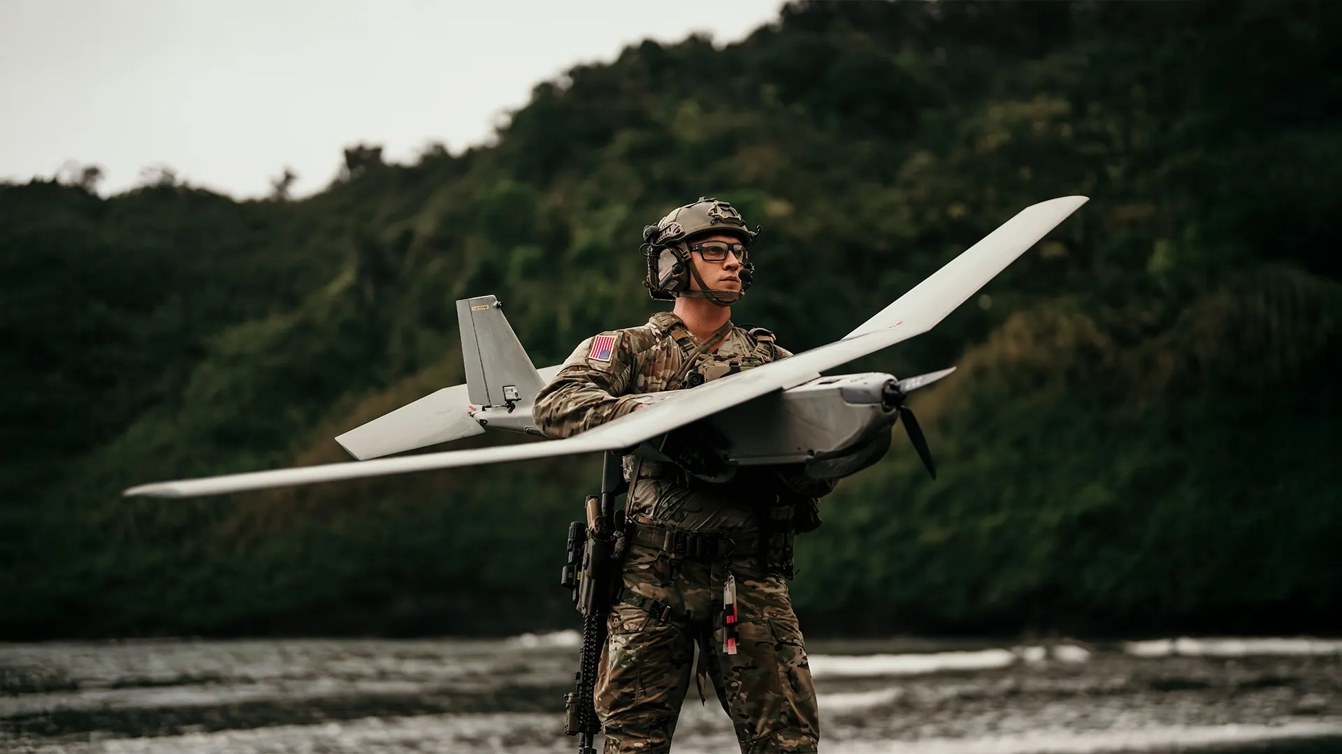 A soldier holding a Puma reconnaissance aircraft beside water
