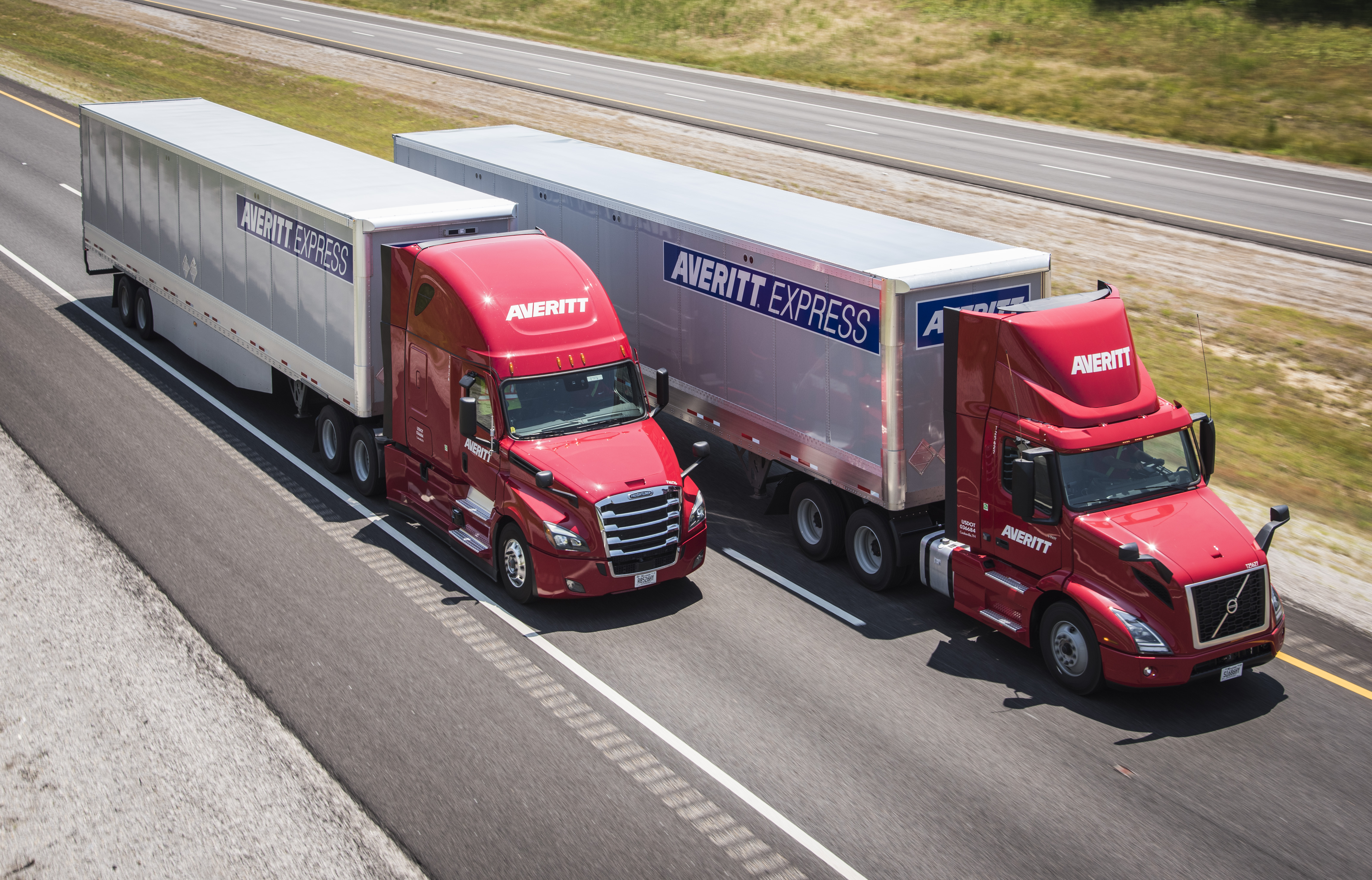 Two red Averitt tractors pulling silver freight trailers on a highway