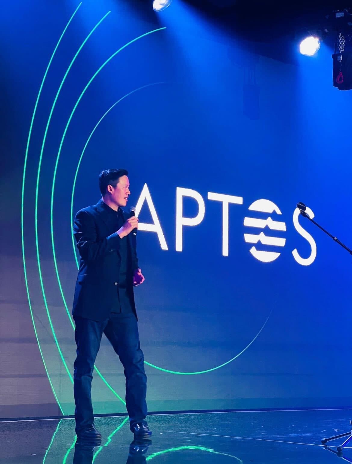 Avery Ching speaking on an Aptos stage under blue lighting