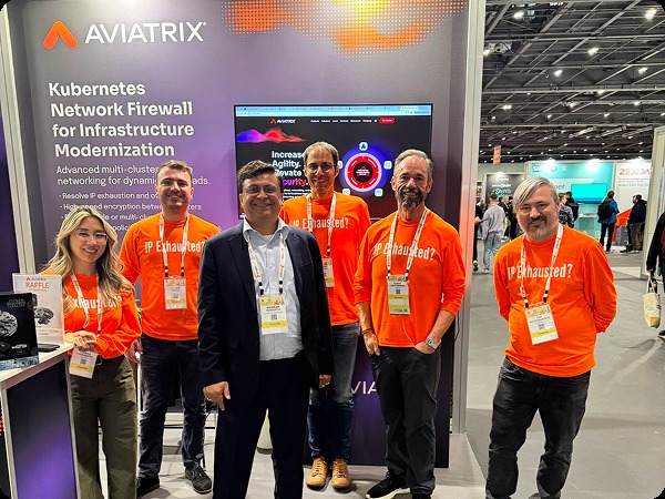 Aviatrix exhibition team in orange shirts beside a Kubernetes network firewall display