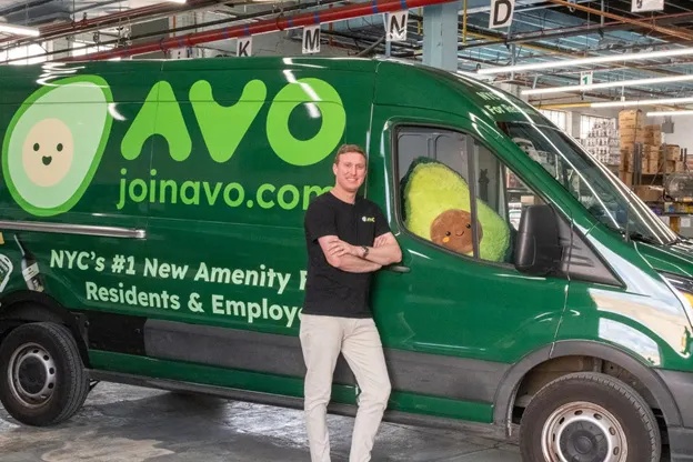 An Avo employee stands beside a green branded delivery van inside a warehouse
