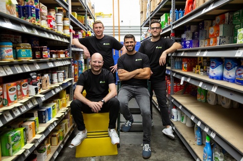 Four Avo team members in black company shirts pose between stocked grocery shelves