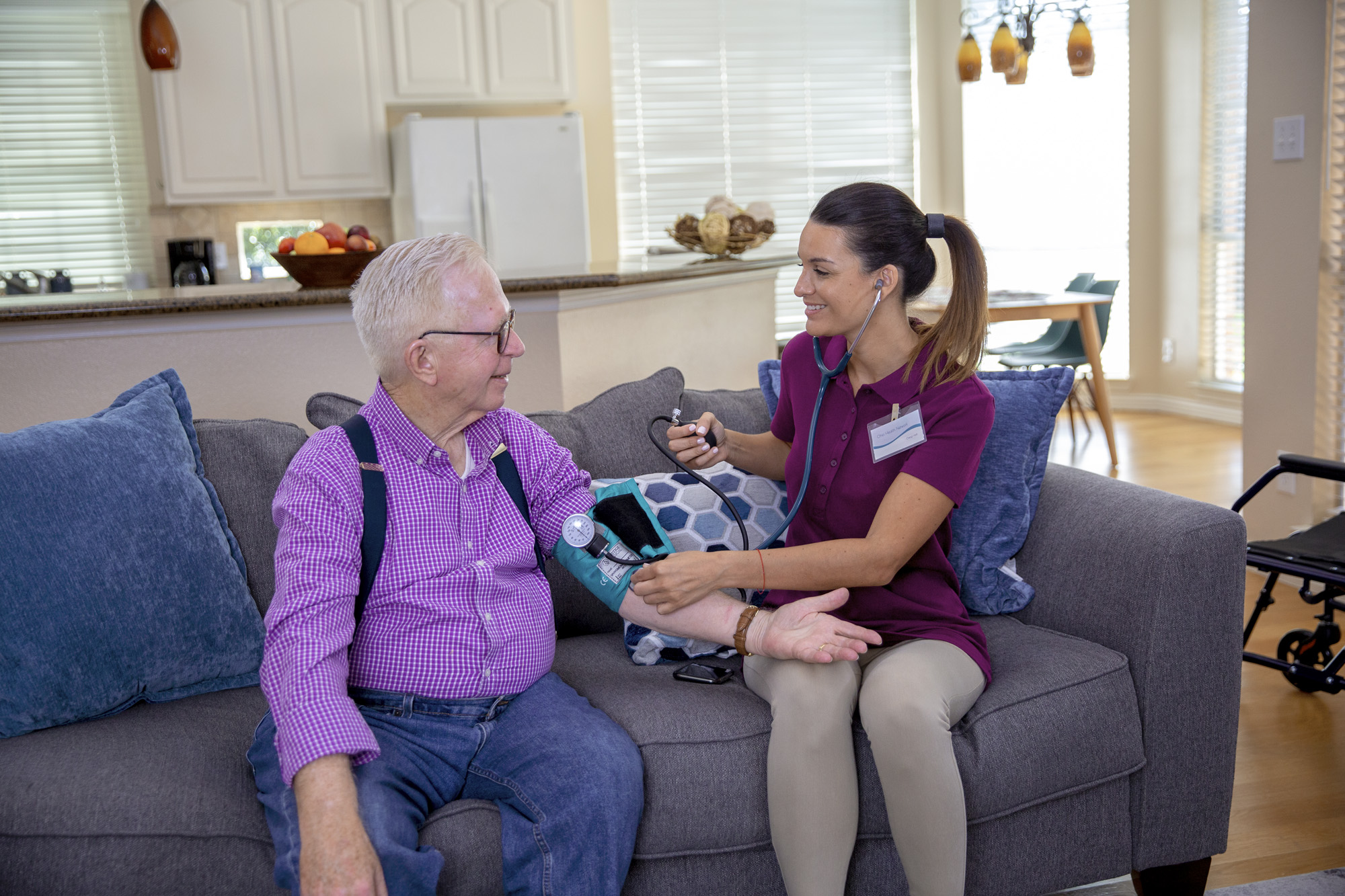 A clinician checks an older man’s blood pressure on a sofa in an Axxess promotional photograph