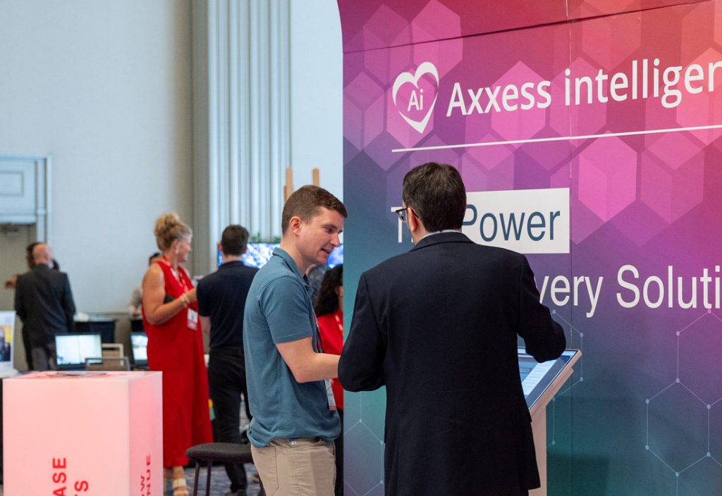 Attendees talk beside a tablet at an Axxess intelligence demonstration area