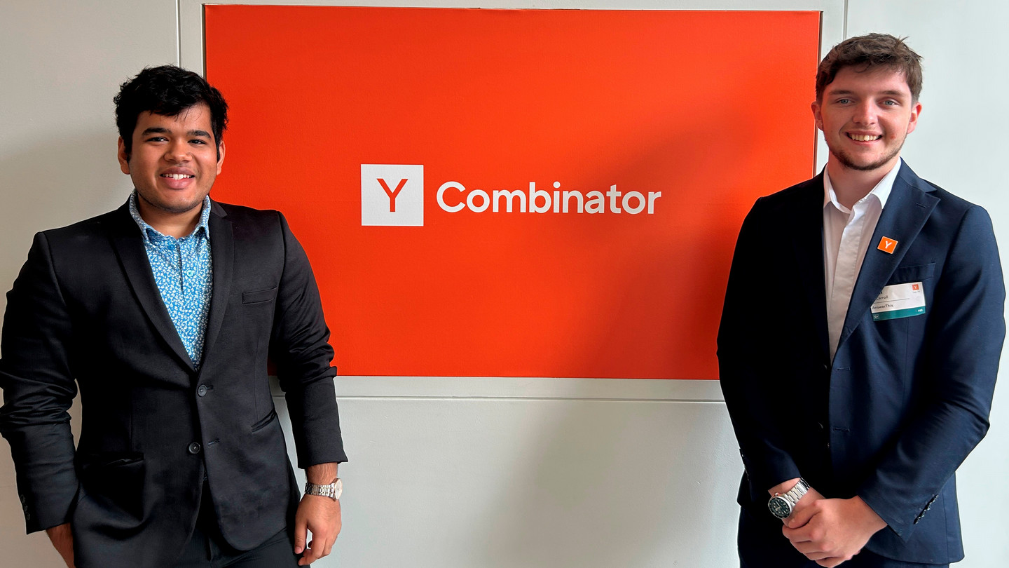 Ayush Garg and Ryan McCarroll standing beside a Y Combinator sign