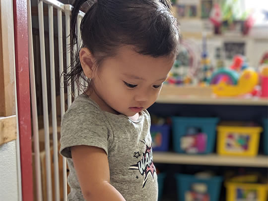 A young child looking down at an activity in a classroom, in an image published by Centres for Early Learning.