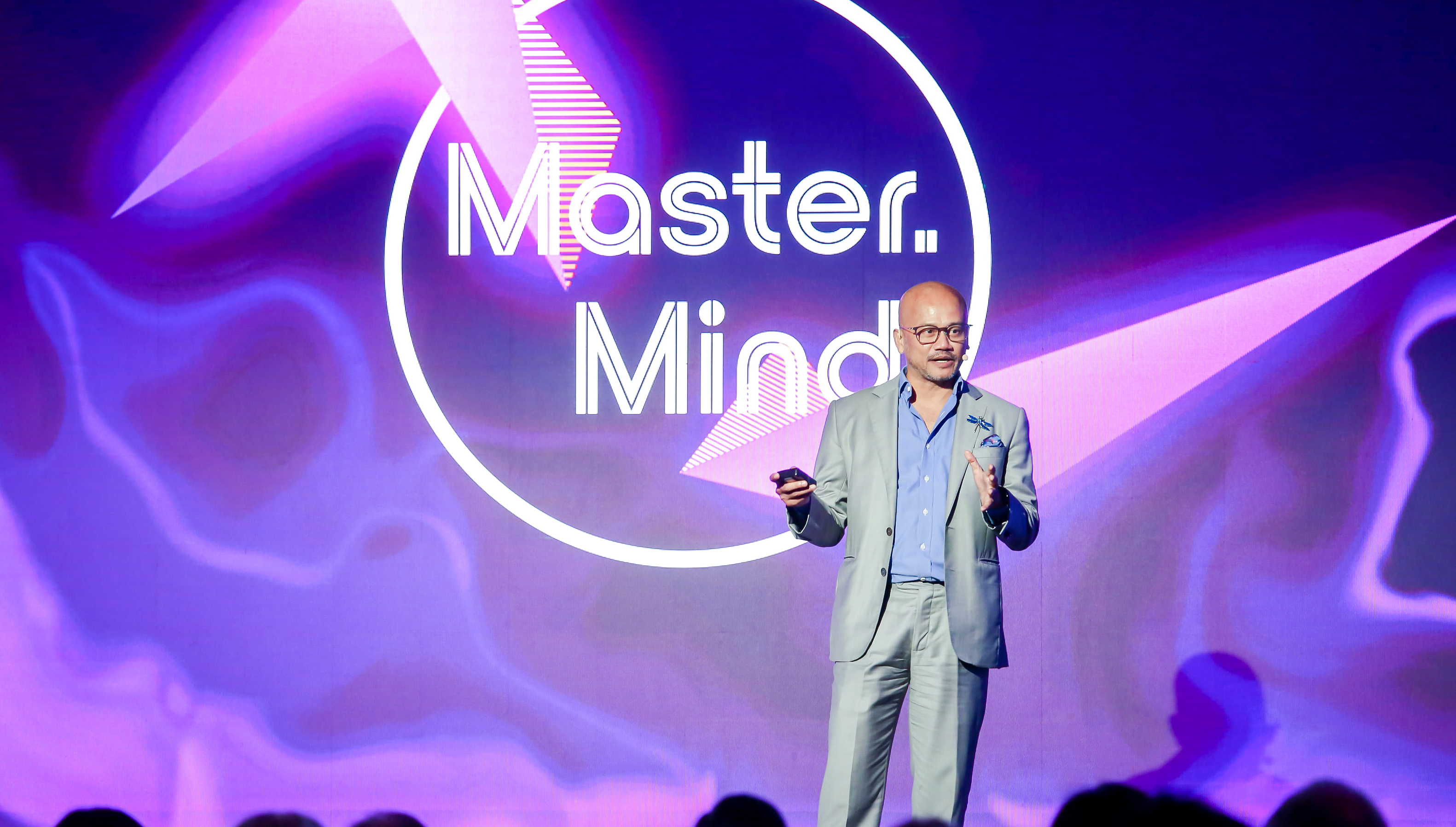 Azran Osman-Rani speaking on stage in a grey suit, with a purple backdrop