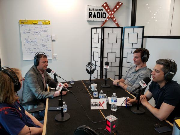 Baha Zeidan, seated on the left in a gray jacket, joins other guests around microphones in the Business RadioX studio