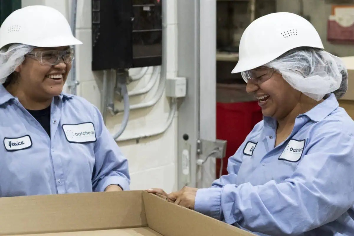 Two Balchem manufacturing employees in protective clothing working beside a cardboard box