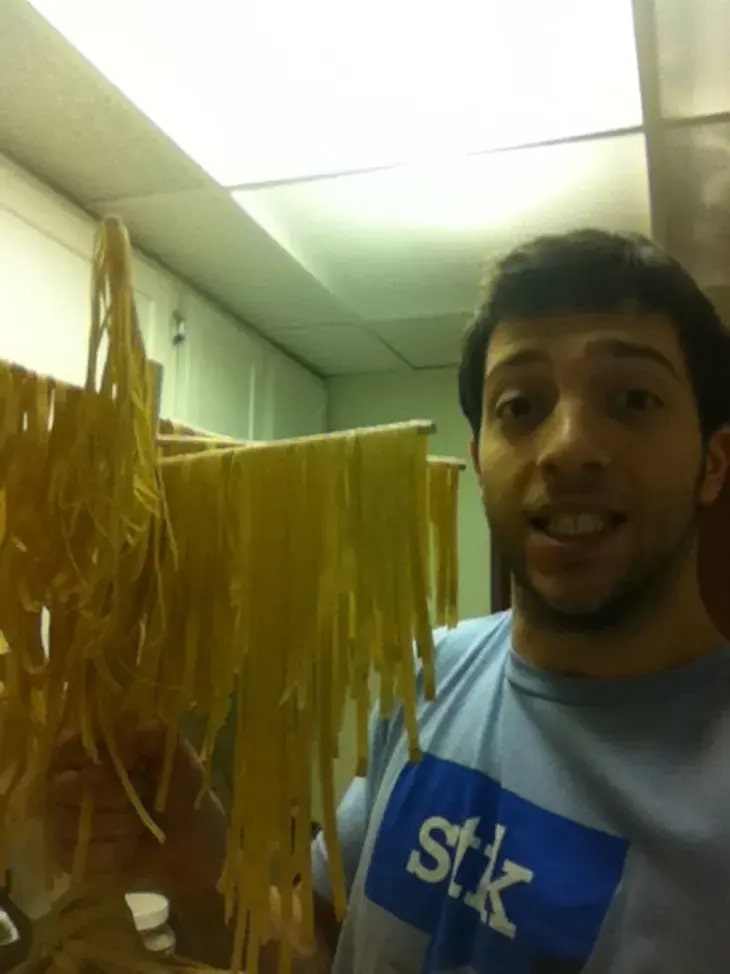 Brian Rudolph holding a rack of early homemade pasta in a kitchen