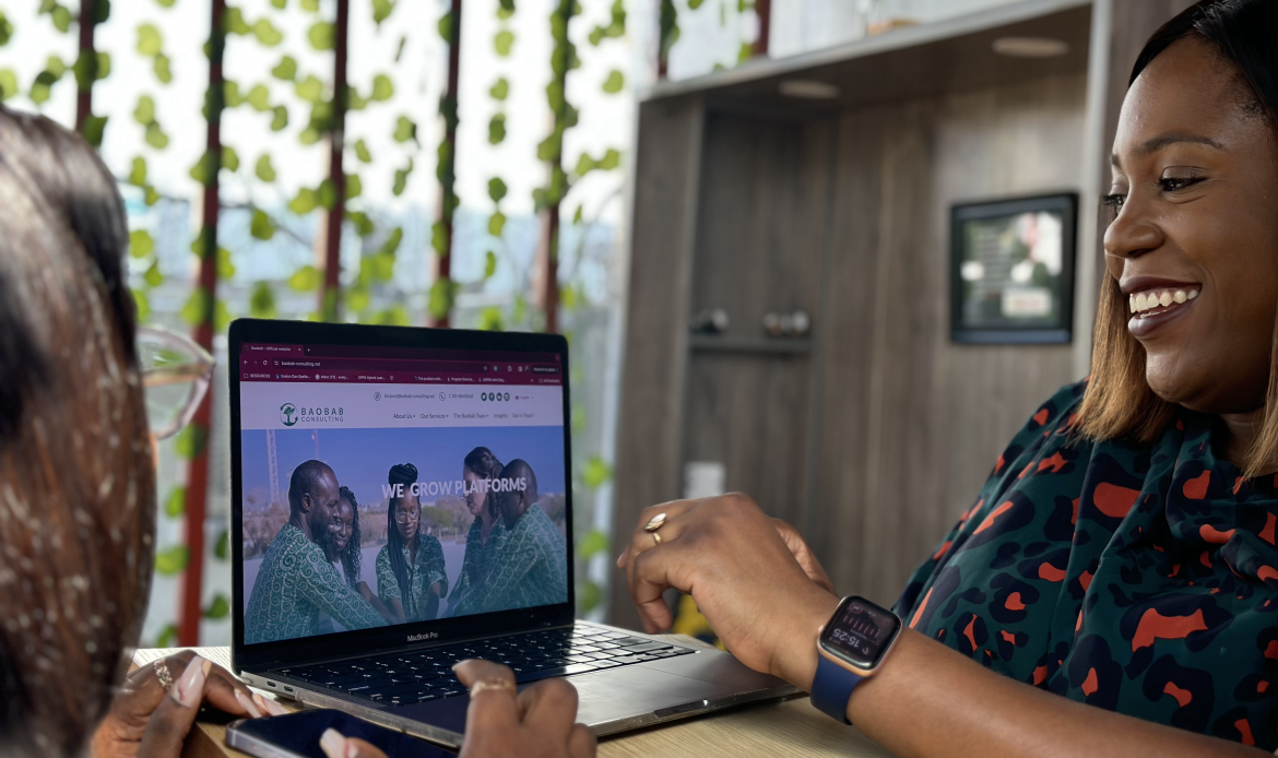 Baobab Consulting colleagues smiling beside a laptop displaying the firm's website
