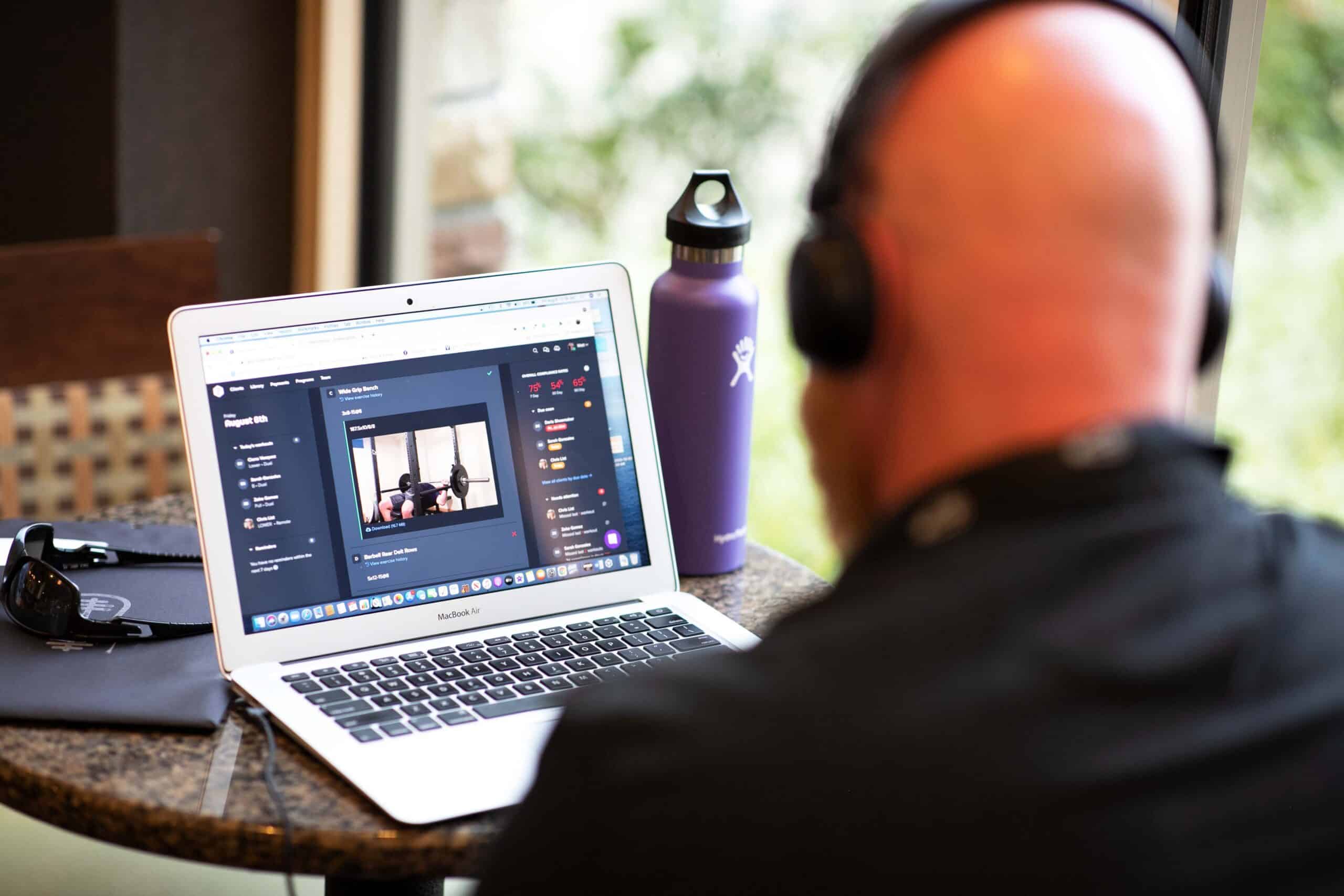 A coach reviewing a client's barbell lift on a laptop