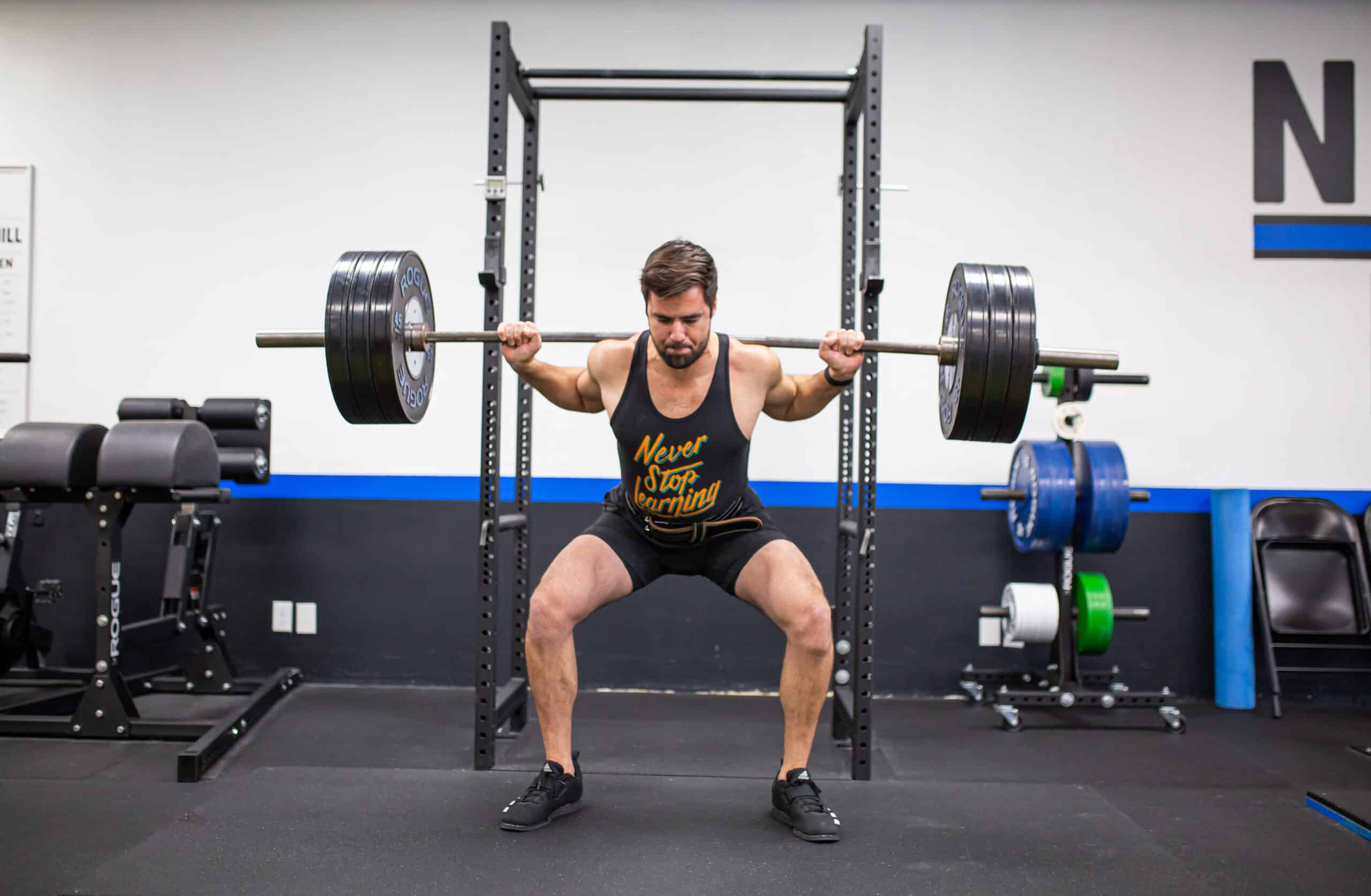A strength athlete performing a barbell squat in a rack
