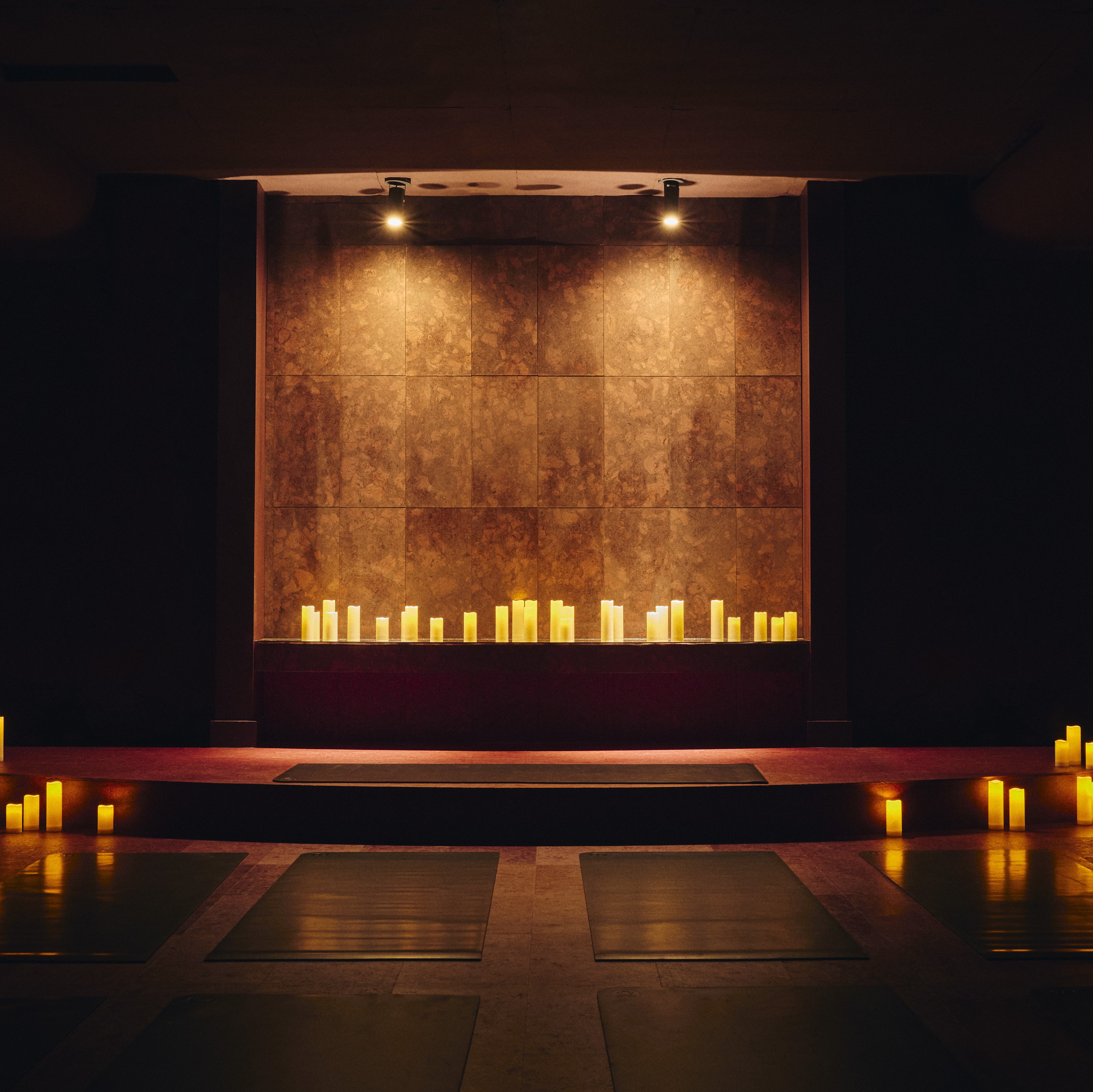 Candlelit Jaybird studio with mats facing a warm brown wall