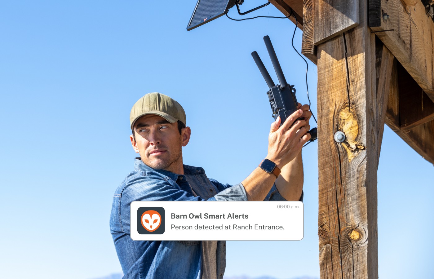 A person mounting a solar-powered Barn Owl camera on a wooden ranch post, with a smart-alert overlay reading Person detected at Ranch Entrance