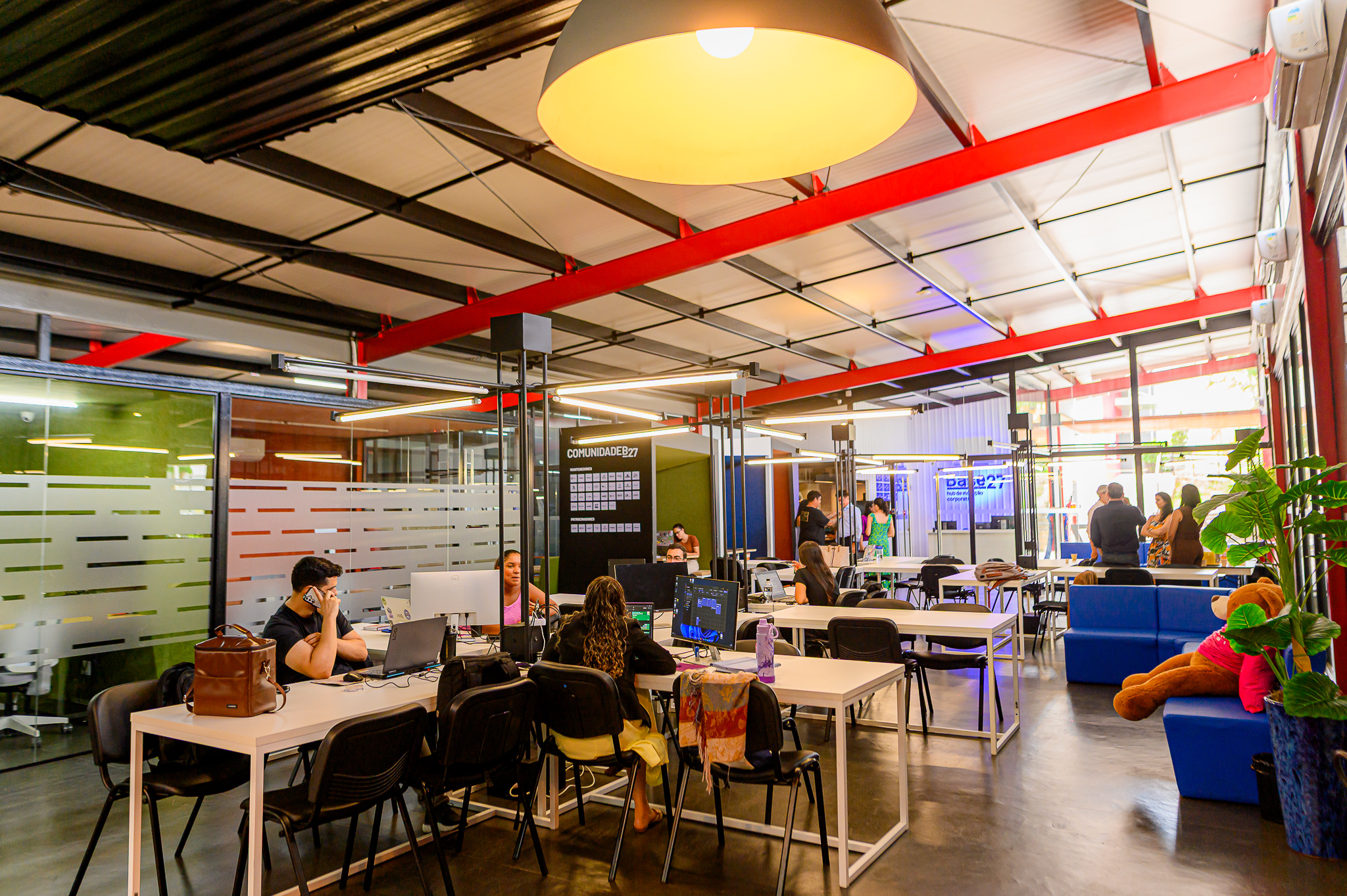 People working at shared desks inside Base27, with meeting rooms and seating nearby