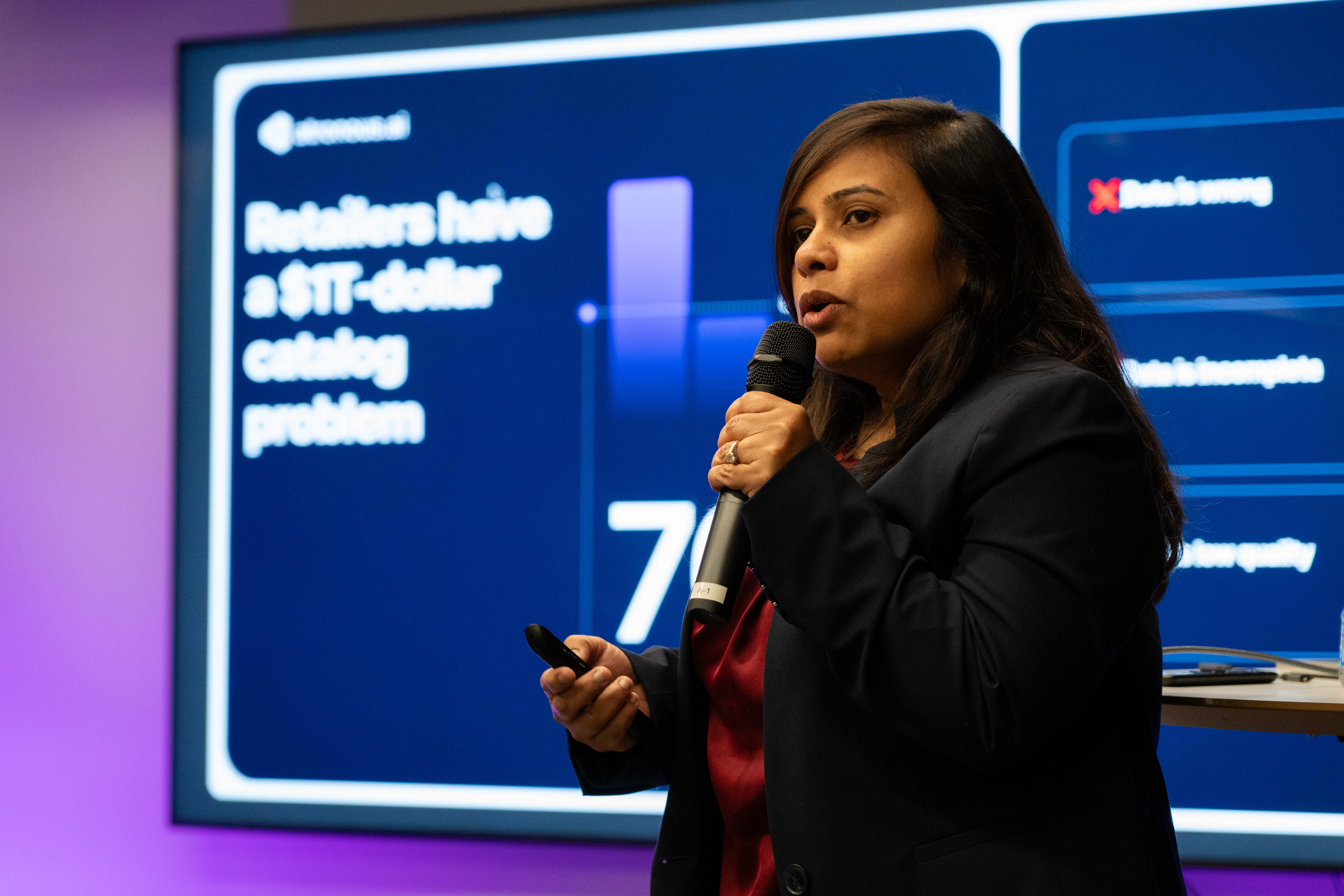 A presenter holds a microphone and clicker in front of a startup pitch slide at a Bay Angels event