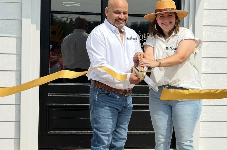 Two people cut a yellow ribbon outside Next Concept Motorsports