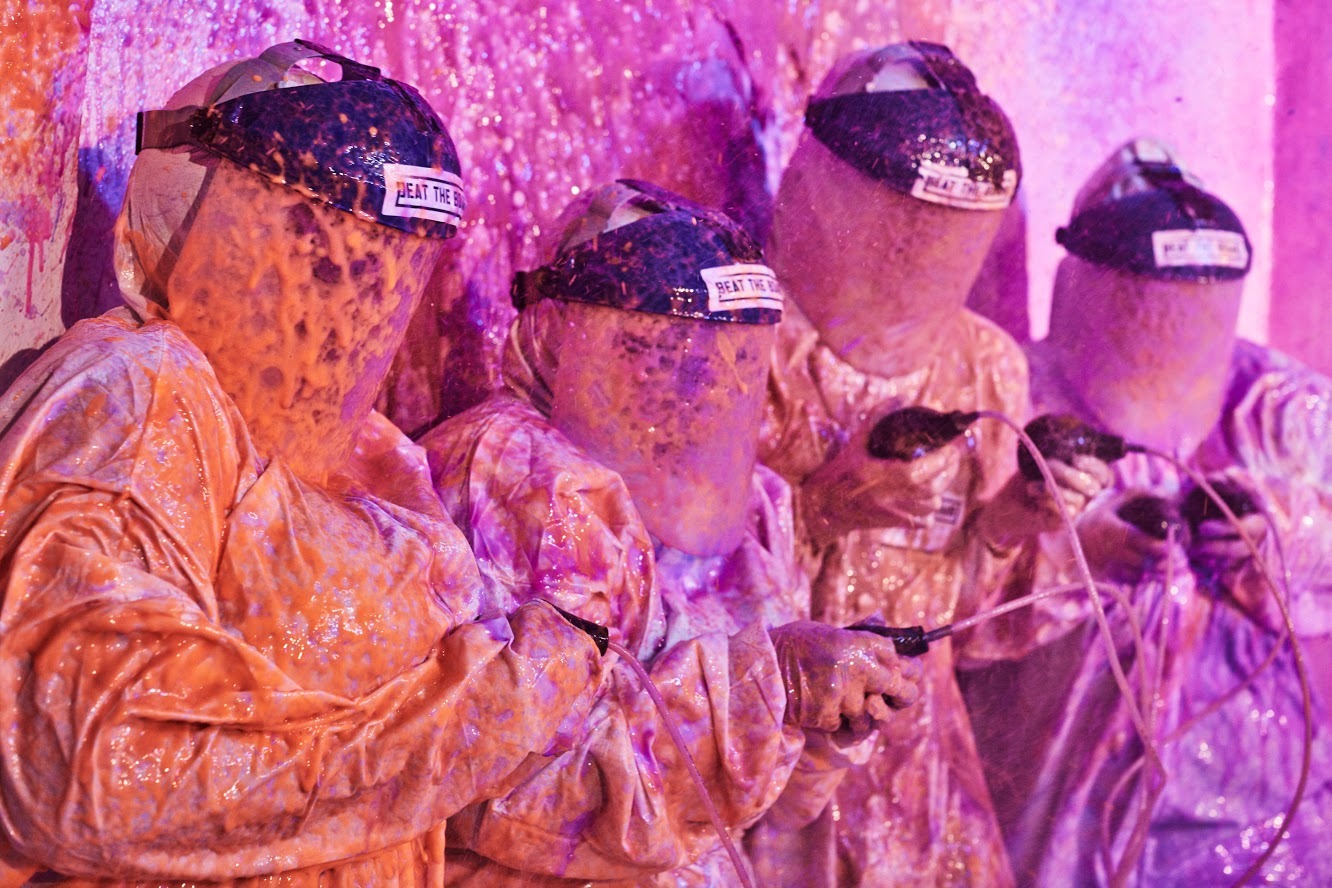BEAT THE BOMB players in hazmat suits inside a high-tech game room